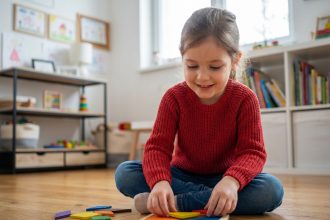 Jeune fille de 5 ans assemble un tangram coloré dans une salle de jeux lumineuse
